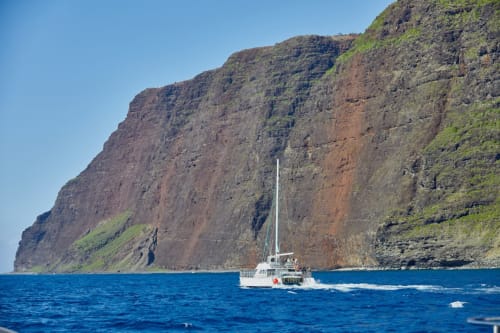 Sailing catamaran off Madeira's volcanic cliffs with clear blue waters near Ribeira Brava