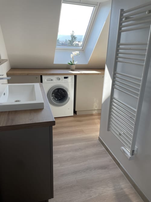 Salle de bains moderne avec lave-linge, lavabo et sèche-serviettes chauffant dans un appartement à Ribeauvillé, vue sur puits de lumière