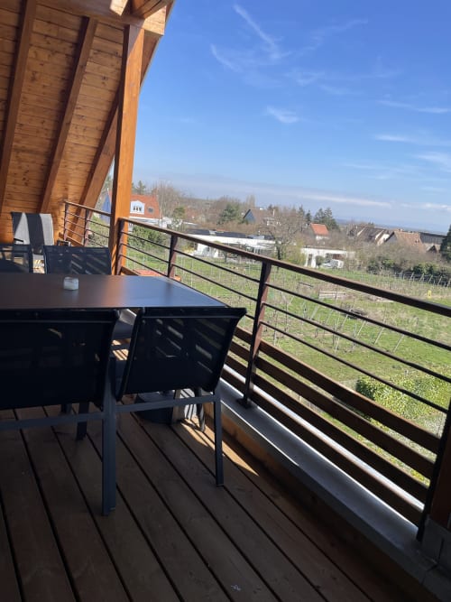 Terrasse en bois avec table et chaises surplombant les vignobles et les maisons du village de Ribeauvillé, ciel bleu dégagé
