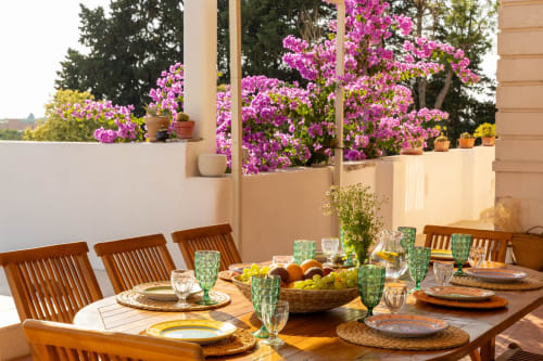 Terrazza esterna di Villa Ceci con tavolo in legno, bicchieri verdi e vibranti fiori di buganvillea rosa, Andria Italia