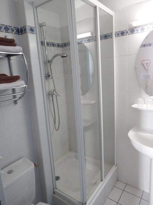Modern bathroom with glass shower enclosure, white tiles, and decorative border at Auberge du Pont de l'Alp hotel