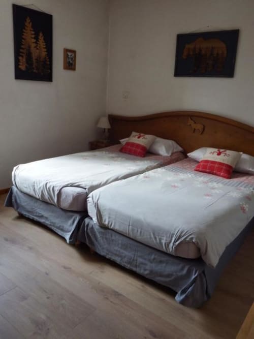 Twin bedroom at Auberge du Pont de l'Alp with white bedding, red pillows, wooden headboard, and mountain artwork in Le