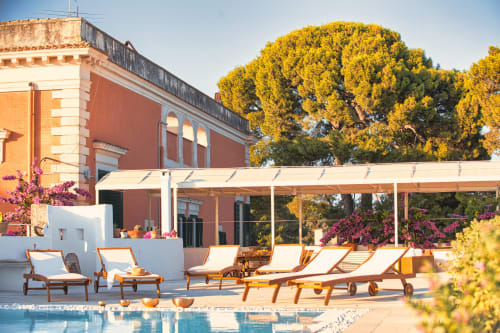 Area lounge con piscina di Villa Ceci ad Andria: edificio in terracotta, lettini, piante fiorite e pergolato ombreggiato