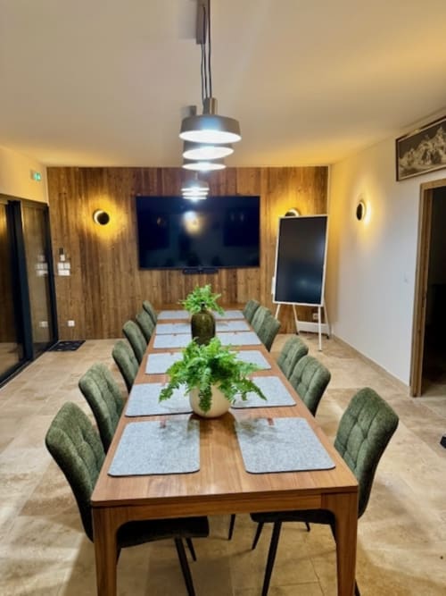 Salle de conférence moderne à la Maison Terre de Lune avec table en bois, chaises vertes et TV murale à Mondragon.