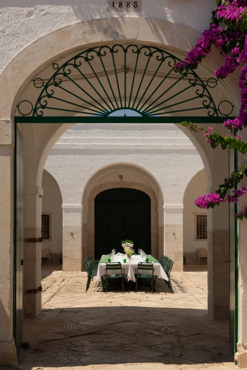 Cortile di Villa Ceci ad Andria con cancello in ferro verde ornamentale, archi in pietra bianca, buganvillea magenta in fiore e setting elegante