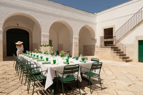 Cortile di Villa Ceci ad Andria con lungo tavolo bianco, sedie verdi e architettura in pietra ad arco sotto cielo azzurro