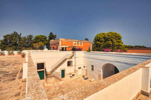 Cortile di Villa Ceci ad Andria con edifici in terracotta, passaggio ad arco e buganvillea fiorita contro il cielo azzurro
