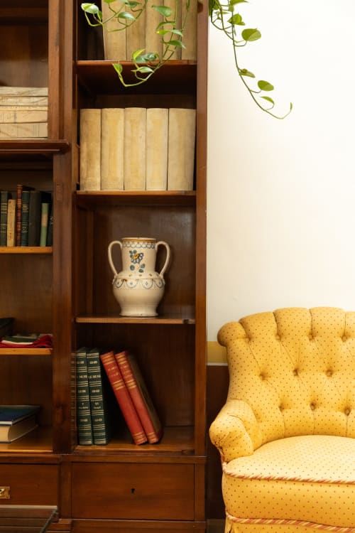 Libreria in legno con vaso decorativo e piante a Villa Ceci Andria, poltrona gialla trapuntata nelle vicinanze