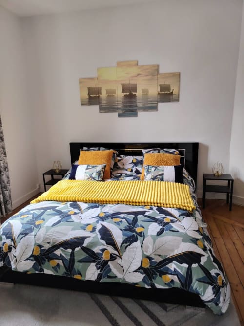 Chambre moderne du gîte Skol en Normandie avec literie florale, plaid jaune et décoration murale bateau à voiles