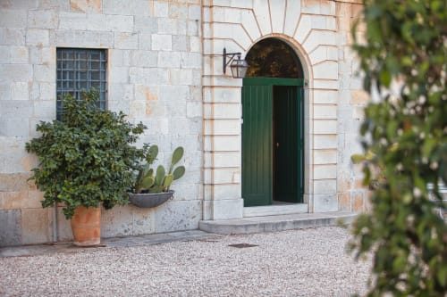 Ingresso di Villa Ceci ad Andria con facciata in pietra, porta ad arco verde, piante in vaso e muri ricoperti di edera