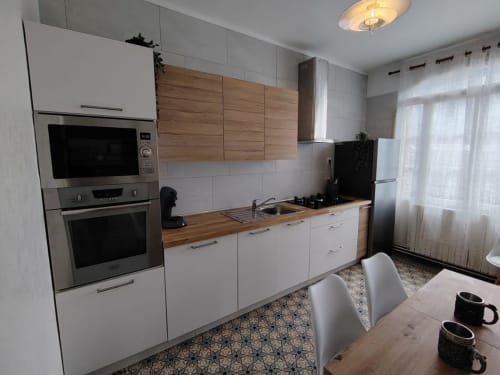 Cuisine moderne du cottage Skol à Rouen avec armoires blanches, plan de travail en bois, électroménagers inox et coin repas