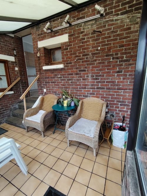 Coin salon sur terrasse avec fauteuils en osier au gîte Skol In Normandy à Rouen, murs de brique et plantes en pots