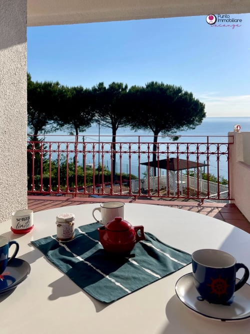 Breakfast table on terrace at Villa Nella, Lanciano with sea view, red teapot, mugs, and coastal landscape