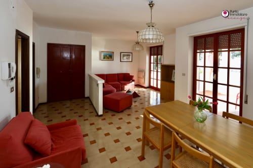 Villa Nella dining and living area with red furniture, wooden table, terracotta tile floors, and French doors in Lanciano,