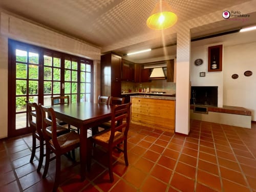 Villa Nella dining area with wood table, kitchen, terracotta floors, and glass doors overlooking garden in Lanciano