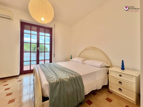 Bright bedroom at Villa Nella in Lanciano with sea view doors, cream bed, wooden nightstand, and rattan ceiling light