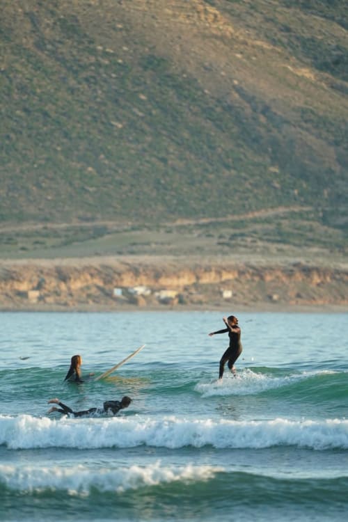 Surfeurs chevauchant les vagues à El Ghazouane, Maroc, avec les montagnes côtières et le village près du Riad Eucalyptus