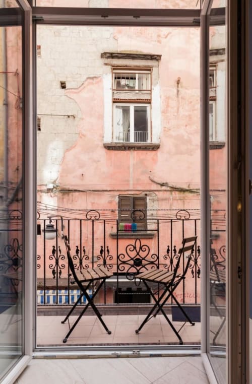 Vista dal balcone della camera TreSette Toledo a Napoli con ringhiera in ferro battuto, sedie e facciata storica rosa