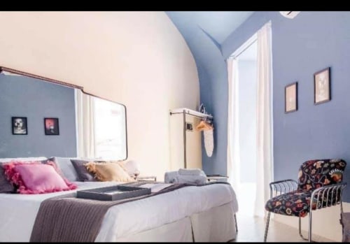 Camera moderna al TreSetti Toledo B&B Napoli con pareti curve blu, letto bianco, cuscini rosa, specchio e sedia a motivi