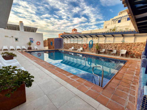 Terraza de piscina de El Faro De Los Genoveses con tumbonas, muros de piedra y pérgola con vistas a la costa de Almería