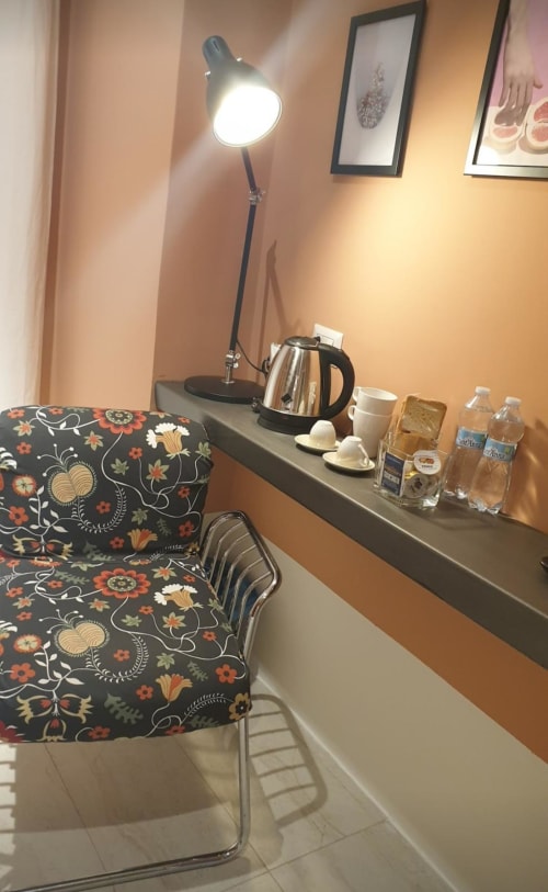 Zona lavoro in camera d'hotel al TreSette Toledo Napoli con lampada da tavolo, bollitore elettrico, tazze e sedia floreale