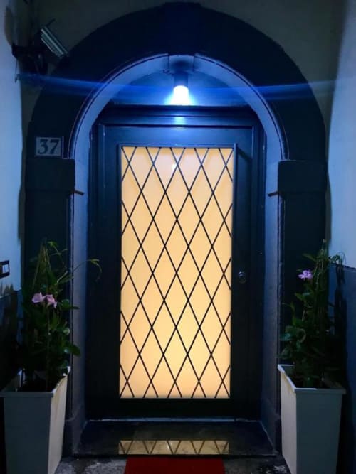 Elegante portale ad arco con vetri a motivo a rombi dell'ingresso dell'appartamento TreSette Toledo Napoli, fiancheggiato da vasi di fiori