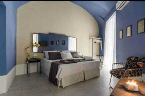 Camera moderna del TreSette Toledo Napoli B&B con pareti blu, letto bianco, specchio e vista sulla città dal balcone