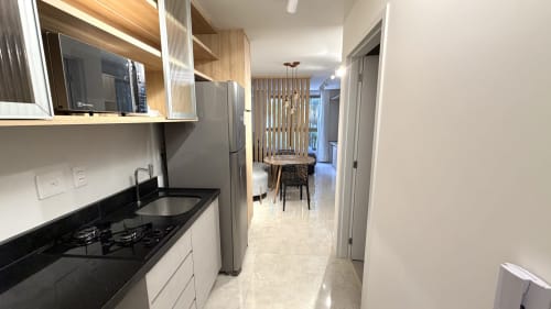 Cozinha moderna em Brasília BnB com eletrodomésticos em aço inoxidável, bancada preta, móveis de madeira e área de refeições