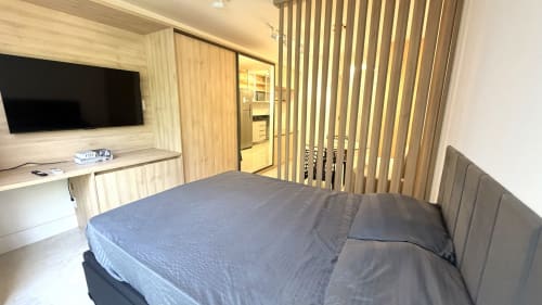 Quarto moderno em Brasília BnB com cama queen, TV de tela plana, acesso à cozinha e persianas verticais na porta da varanda.