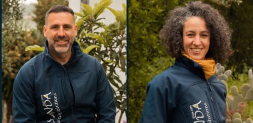 Two smiling staff members in navy jackets at Escanda Building Solutions hotel in Spain, outdoors among plants