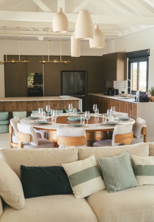 Cuisine ouverte et salle à manger modernes avec table ronde en bois, canapé crème, rangements foncés et luminaires suspendus à la Villa