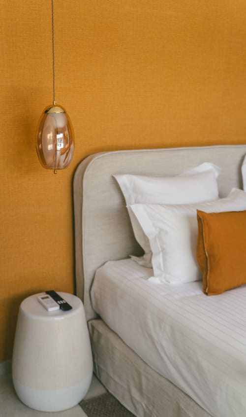 Chambre moderne de la Villa Rheia, Collection Blue Horizon, avec mur d'accent doré-orange, luminaire suspendu et lit rembourré crème