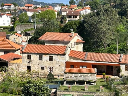 Hotel rural Casa Rural A Bouciña en Hío, España con edificios de piedra y tejados de barro rodeados de verde campiña