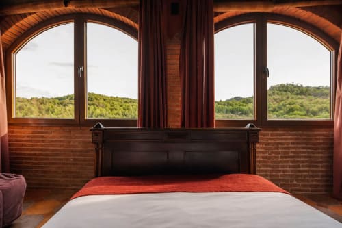 Cama frente a ventanas arqueadas con vistas al bosque