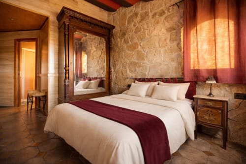 Habitación de piedra con cama doble y armario clásico con espejo junto a una ventana.