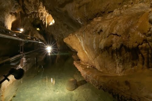 Camera sotterranea della Grotta di Casa Scola a Loano con formazioni calcaree illuminate e specchio d'acqua immobile.