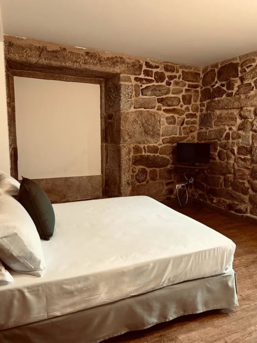 Dormitorio rústico de piedra en Casa Rural A Bouciña con cama blanca y muebles de madera en Hío