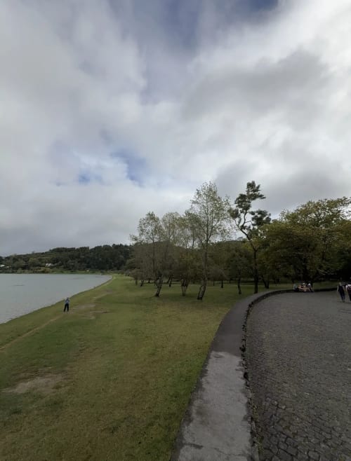 Lakeside park at Golden Mermaid Villa in Ribeirinha with walking path, green lawns, and trees under cloudy sky