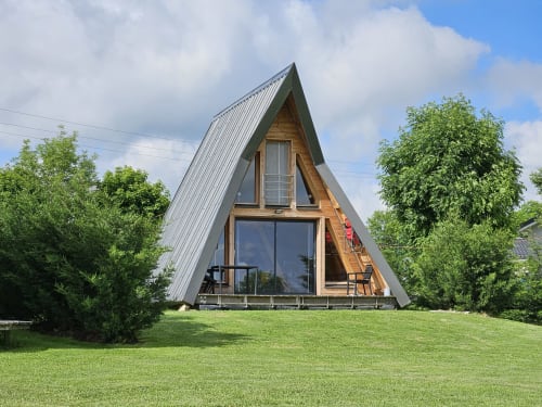 Cabine contemporaine La Cocotte à Logis Las Crozas à Vernines, avec toit en métal et grandes fenêtres, entourée de pelouse verdoyante