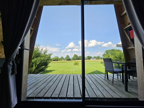 Vue depuis la chambre La Cocotte du Logis Las Crozas offrant un paysage champêtre paisible avec champs verts et ciel depuis la terrasse en bois