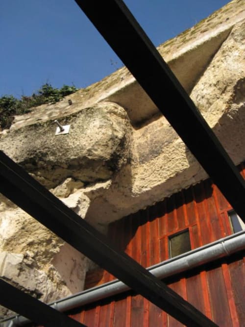 Historic stone troglodyte structure with modern orange corrugated metal addition at Les Troglos de Beaulieu, France