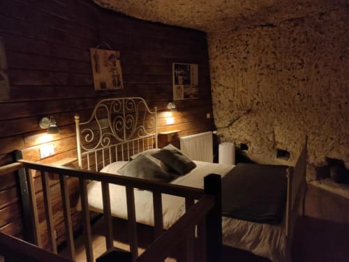 Cozy bedroom at Les Troglos de Beaulieu with ornate metal bed, warm lighting, cork walls, and rustic charm in