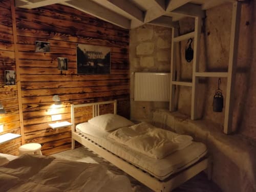 Rustic troglodyte bedroom at Les Troglos de Beaulieu with wooden walls, bed, and carved stone alcoves
