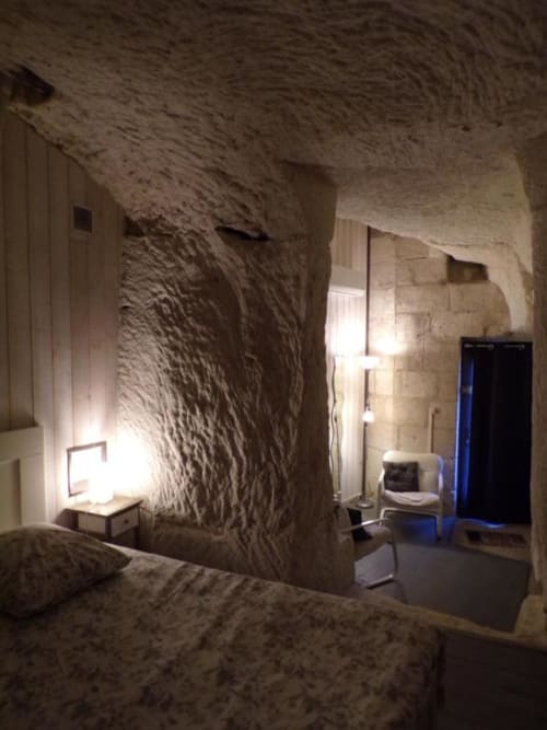 Rustic stone bedroom in Les Troglos de Beaulieu with textured walls, bed, nightstand, chair, and blue door