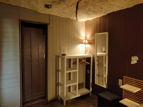 Chambre des Troglos de Beaulieu avec plafond en pierre, étagères en bois, lampe et murs bordeaux foncé