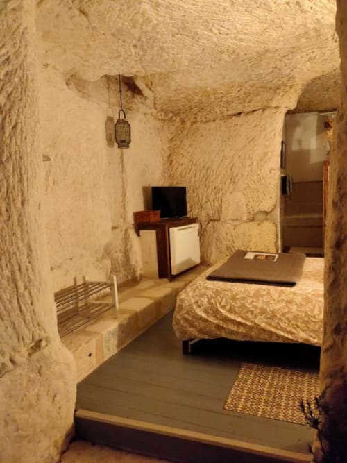 Rustic cave bedroom at Les Troglos de Beaulieu with stone walls, bed, desk, and hanging lantern in Beaulieu-les-Loches,