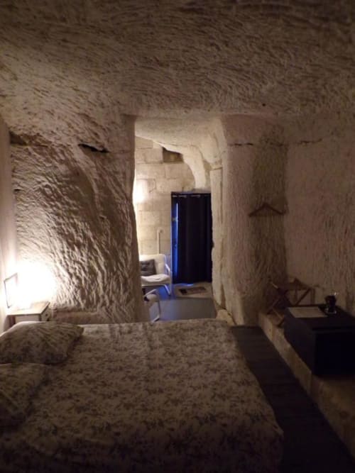 Stone troglodyte room at Les Troglos de Beaulieu with rustic walls, blue door, and modern furnishings in Beaulieu-les-Loches
