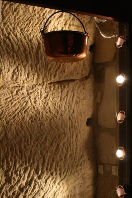 Rustic stone wall with copper cauldron and ambient lighting at Les Troglos de Beaulieu troglodyte accommodation
