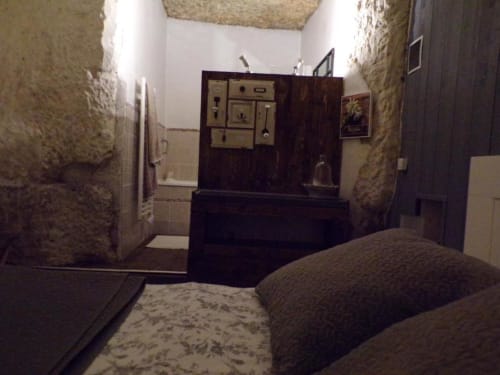 Rustic troglodyte bedroom at Les Troglos de Beaulieu with stone walls, dark wood furniture, and garden view