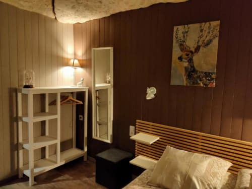 Chambre cosy aux Troglos de Beaulieu avec tête de lit en lattes de bois, étagères blanches et plafond aux poutres rustiques